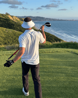 Man holding club with white brim hat facing ocean