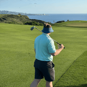 Man golfing with iron on shoulder looking at ocean